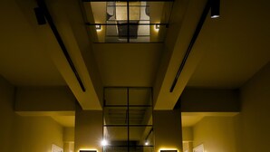 Eine Hotelhalle mit einer Rezeption, zwei Sesseln und einer Bank. Zwei beleuchtete Schilder zeigen Telefonnummern.