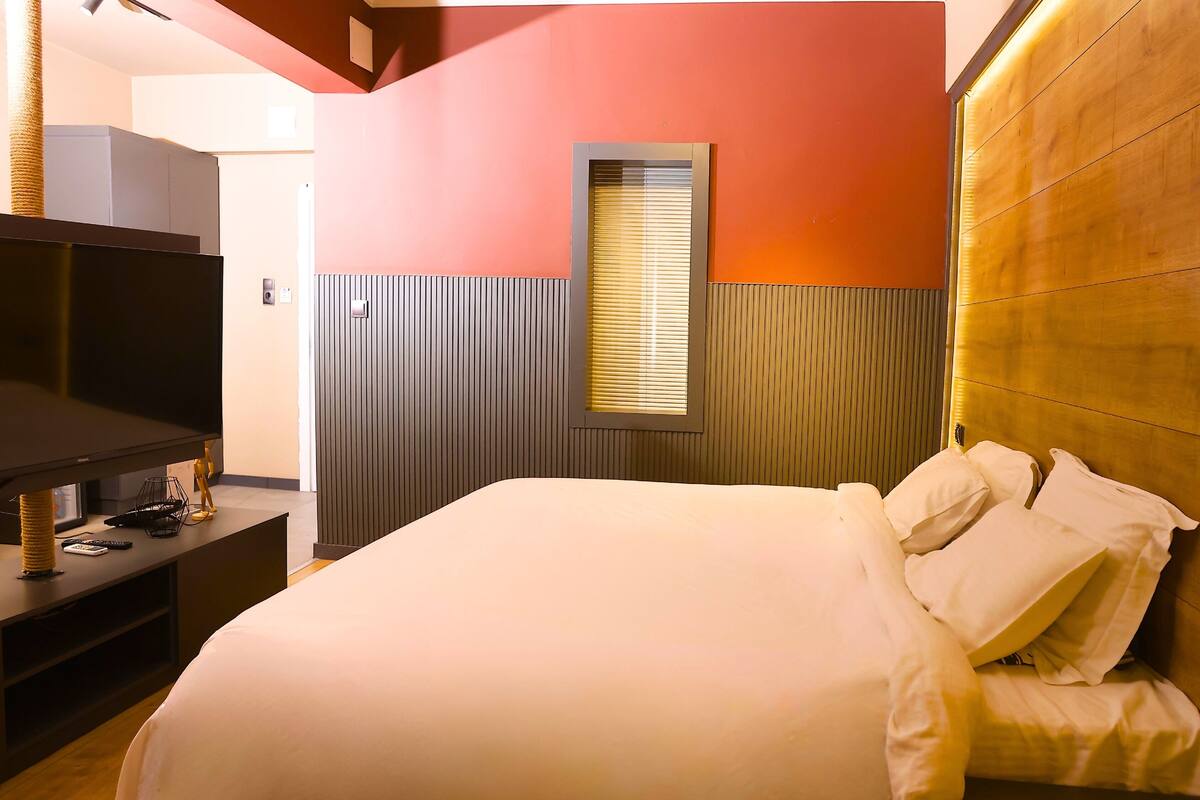 Una habitación de hotel moderna con una cama grande, un televisor de pantalla plana y un cabecero de madera.