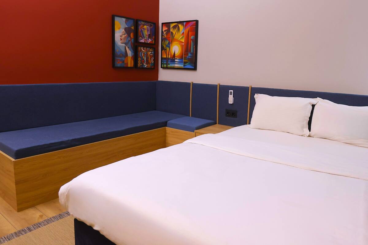 Habitación de hotel con una cama grande, un banco empotrado en la pared y dos cuadros colgados.