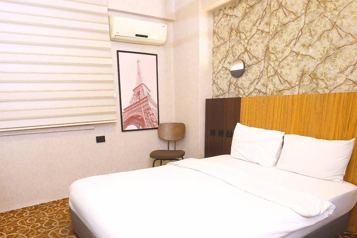 Una habitación de hotel con una cama, una silla, un armario y aire acondicionado instalado en la pared.