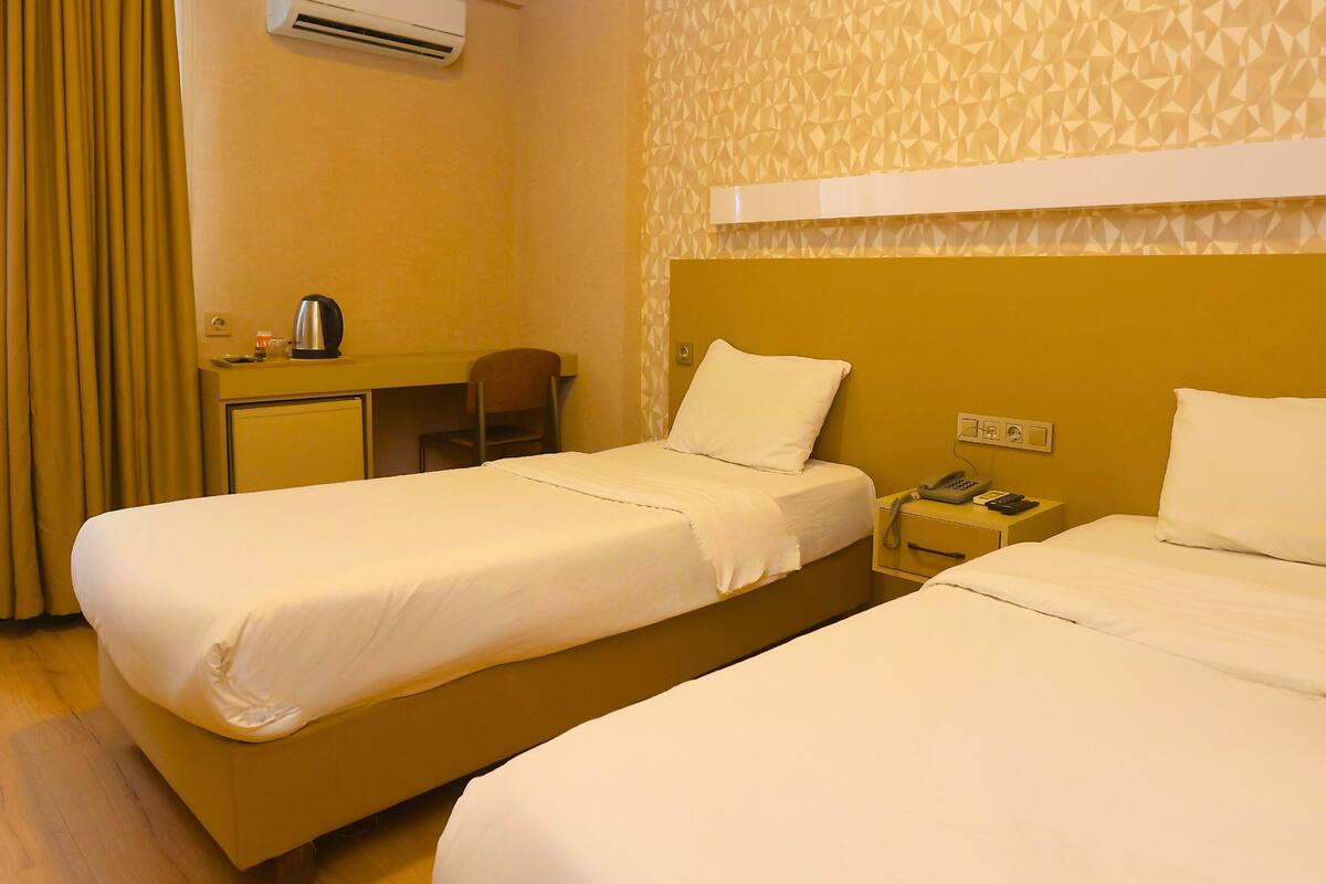 Habitación de hotel con dos camas, un escritorio, una silla, un equipo de aire acondicionado y una pared con estampado.