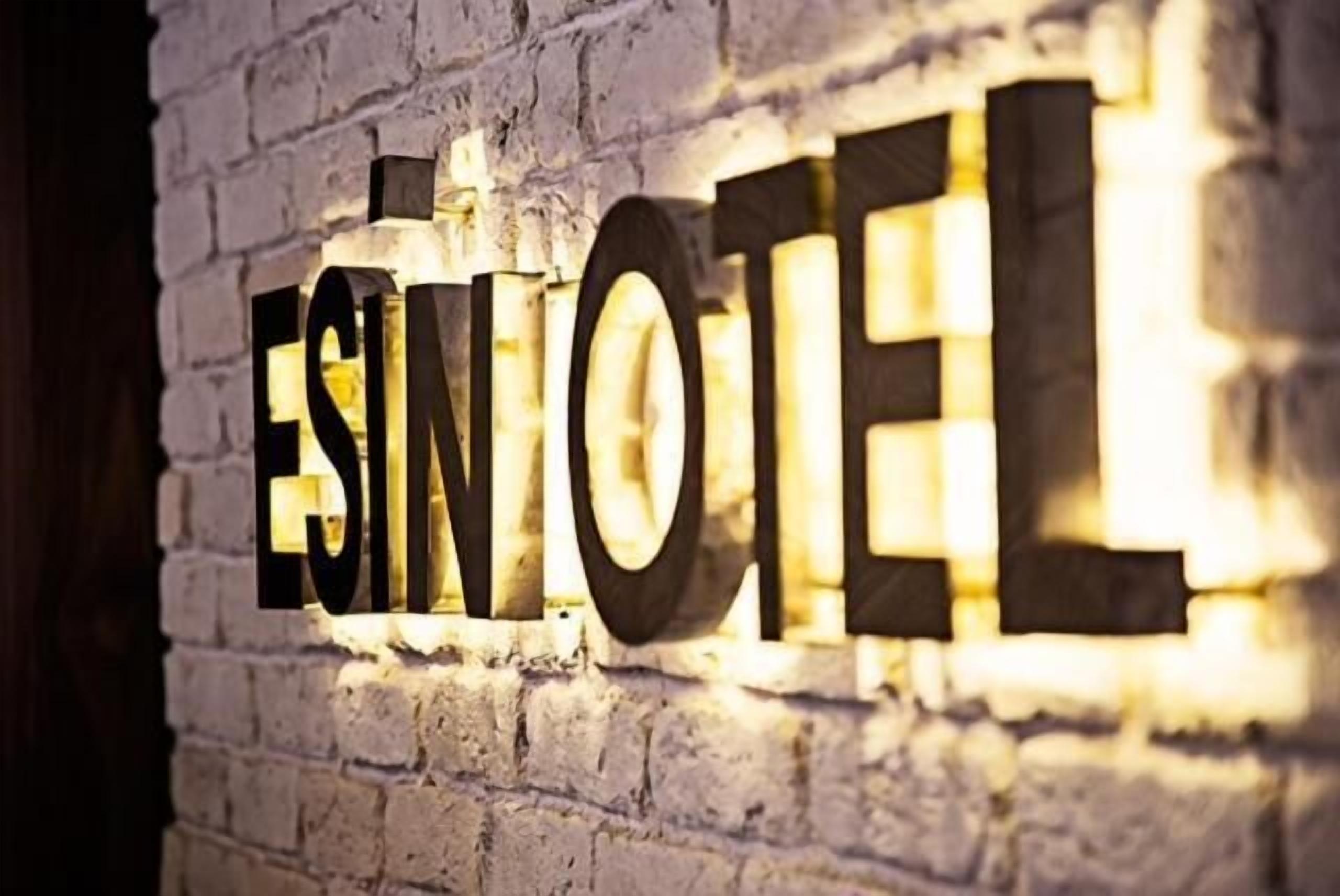 Illuminated letters spelling "ESINOTEL" on a brick wall.