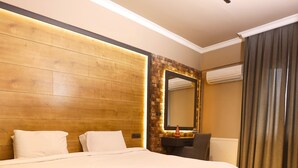 Ein Hotelzimmer mit einem großen Bett, einem hölzernen Kopfteil, einem Spiegel, einem Schreibtisch und einem Fenster mit Vorhängen.