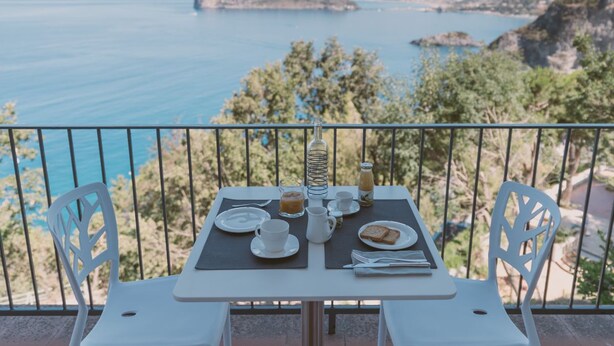 A table set on a balcony overlooking a coastal view with mountains in the distance. - Villa Crawford (San Nicola Arcella)