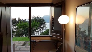 A room with a desk, a lamp, and a large window overlooking a body of water and greenery. - Villa Crawford (San Nicola Arcella)