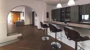 A modern kitchen with a bar area, featuring dark wood cabinets, a stainless steel countertop, and three bar stools. - Villa Crawford (San Nicola Arcella)