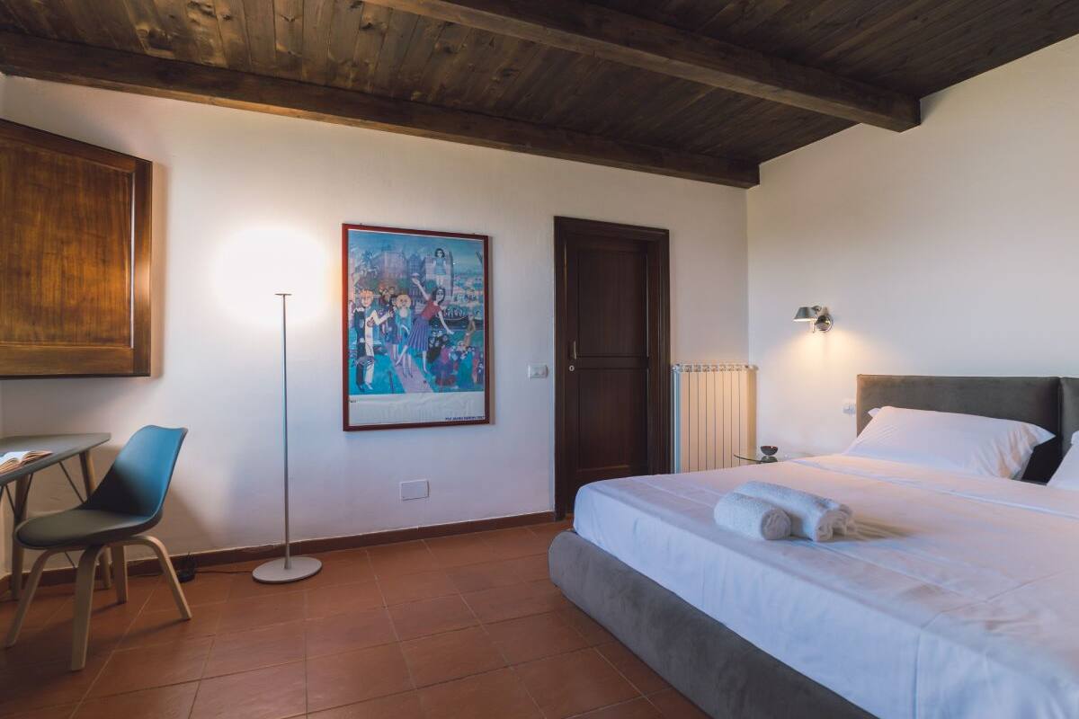 Um quarto com cama, uma poltrona, um abajur, uma porta e um quadro na parede.