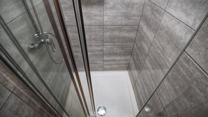 A glass-enclosed shower stall with a handheld showerhead, a white soap dish on the wall, and a tiled floor. - Urban Beach I (Portimão)