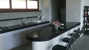 A modern kitchen with a central island, bar stools, a coffee machine, and a window above the sink. - 2 Bedroom Seaview Villa Laurenz (Koh Samui)