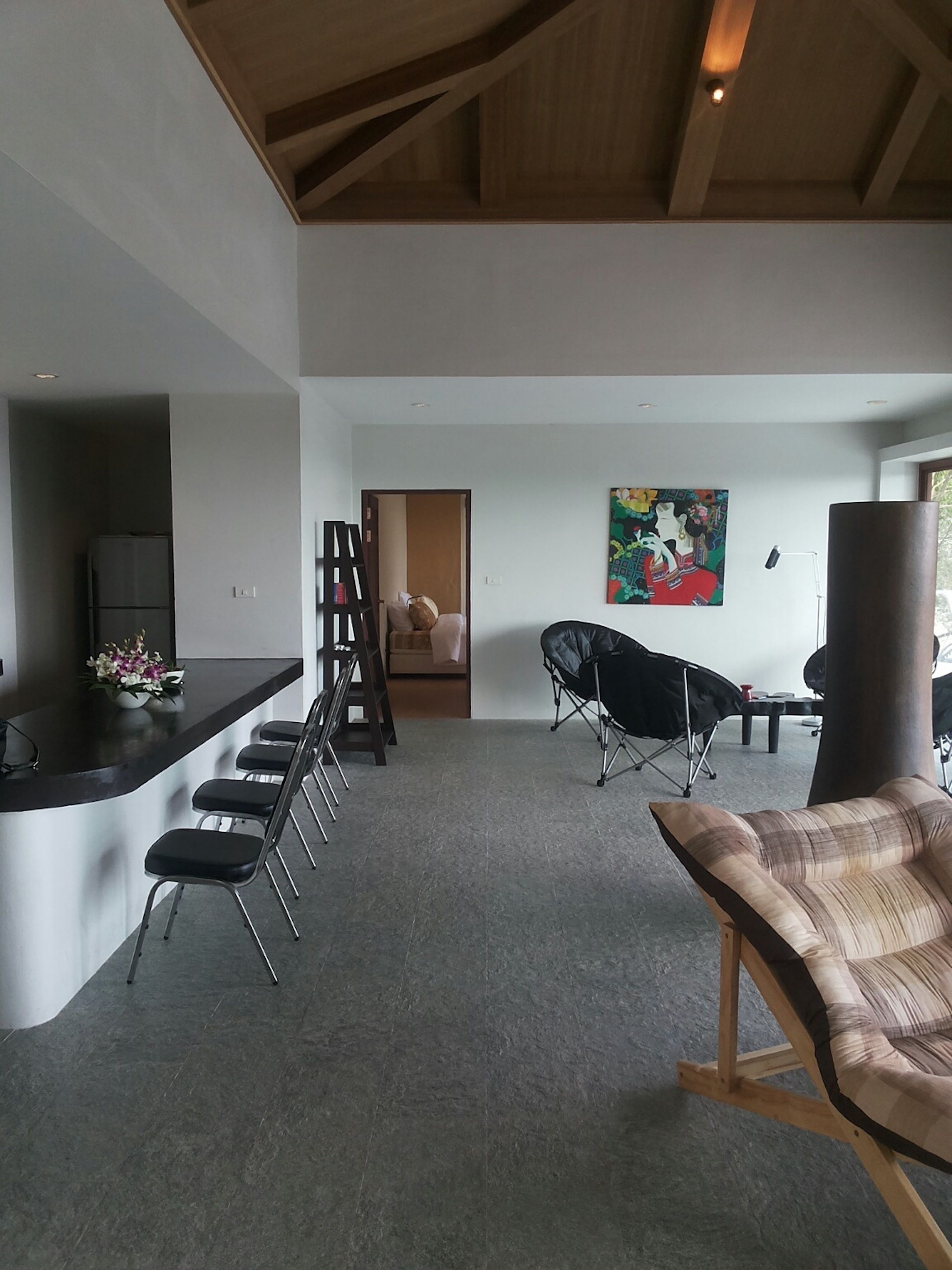 A modern kitchen with a bar area, a dining space with chairs, a sofa, and a colorful painting on the wall.