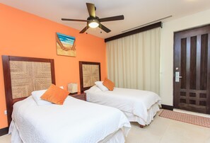 A hotel room with two beds, a ceiling fan, a painting, and a door.