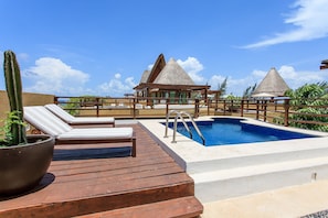 A wooden deck with lounge chairs, a swimming pool, and thatched-roof structures.