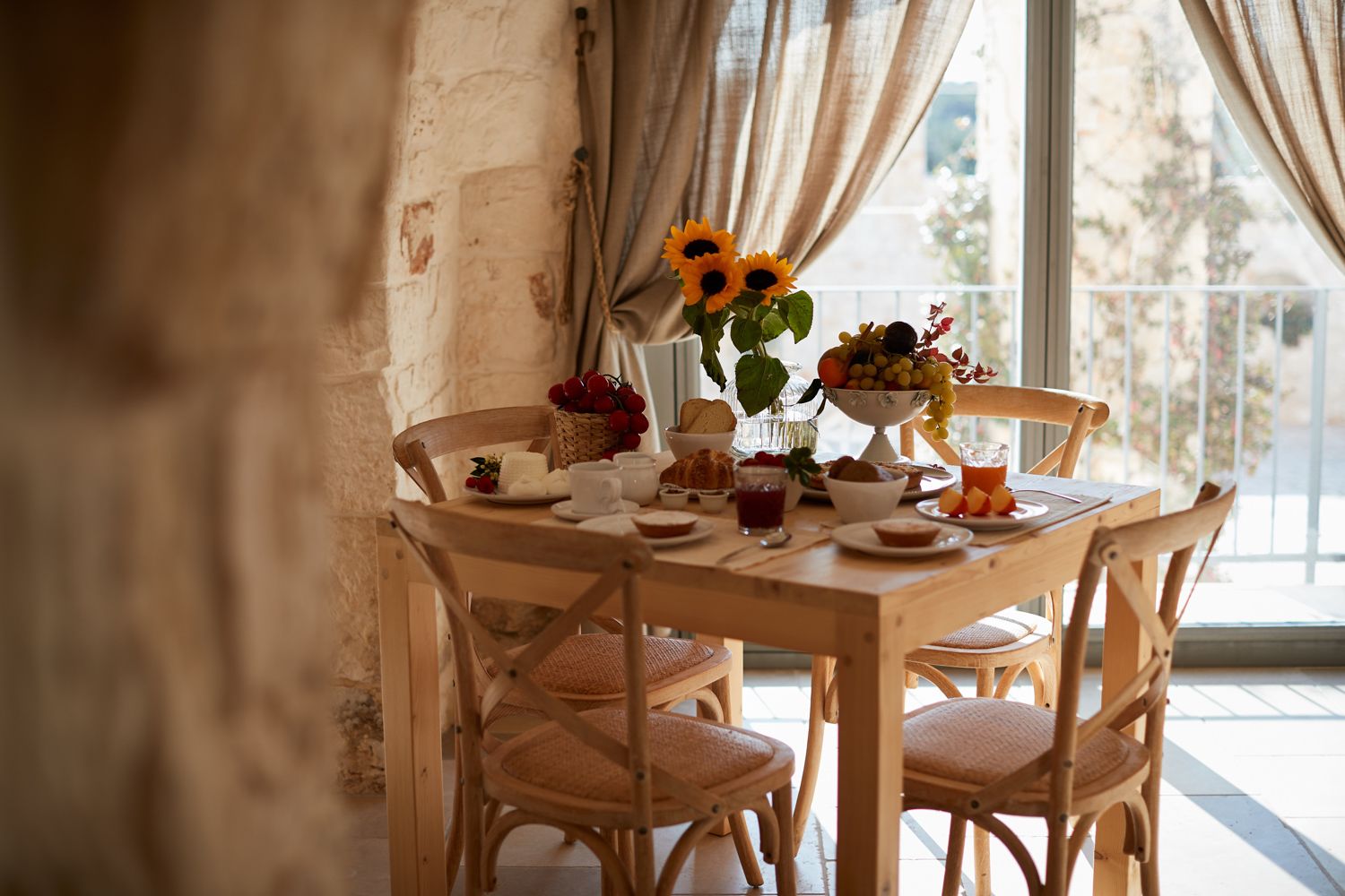 Una mesa de madera con sillas, un jarrón con girasoles y un frutero.