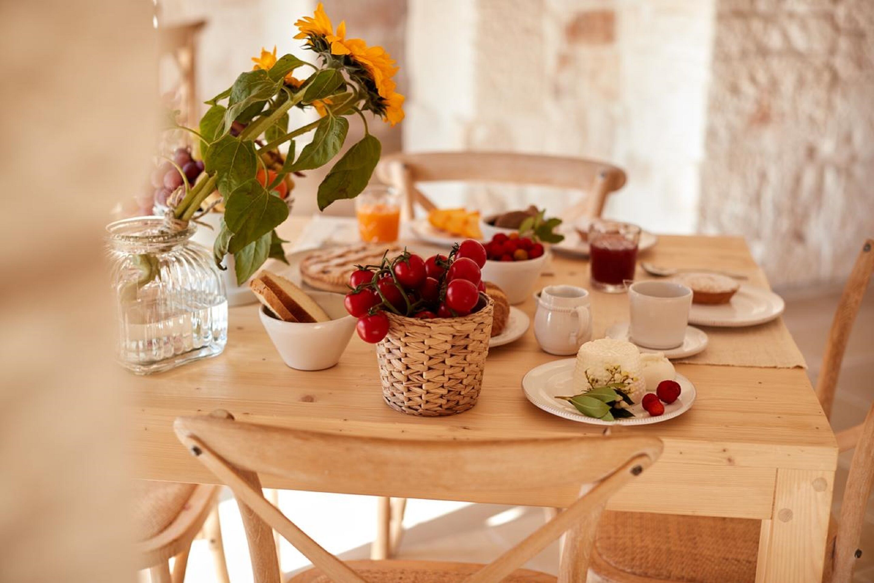 A wooden dining table with a vase of sunflowers, a basket of cherries, and various dishes and drinks.