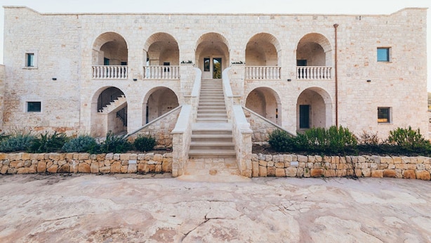 Un edificio con una escalera central que conduce a una entrada, rodeado de muros de piedra y ventanas de arco.