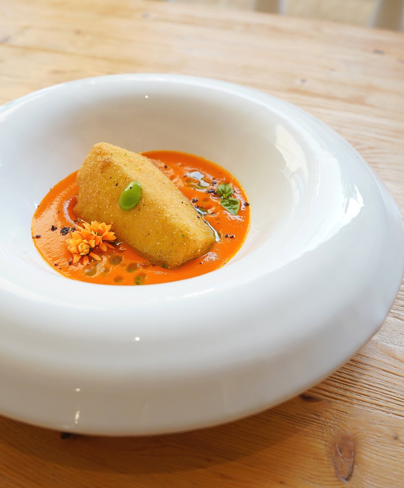 Un plato blanco con un solo alimento, quizás una croqueta, sobre una mesa de madera.