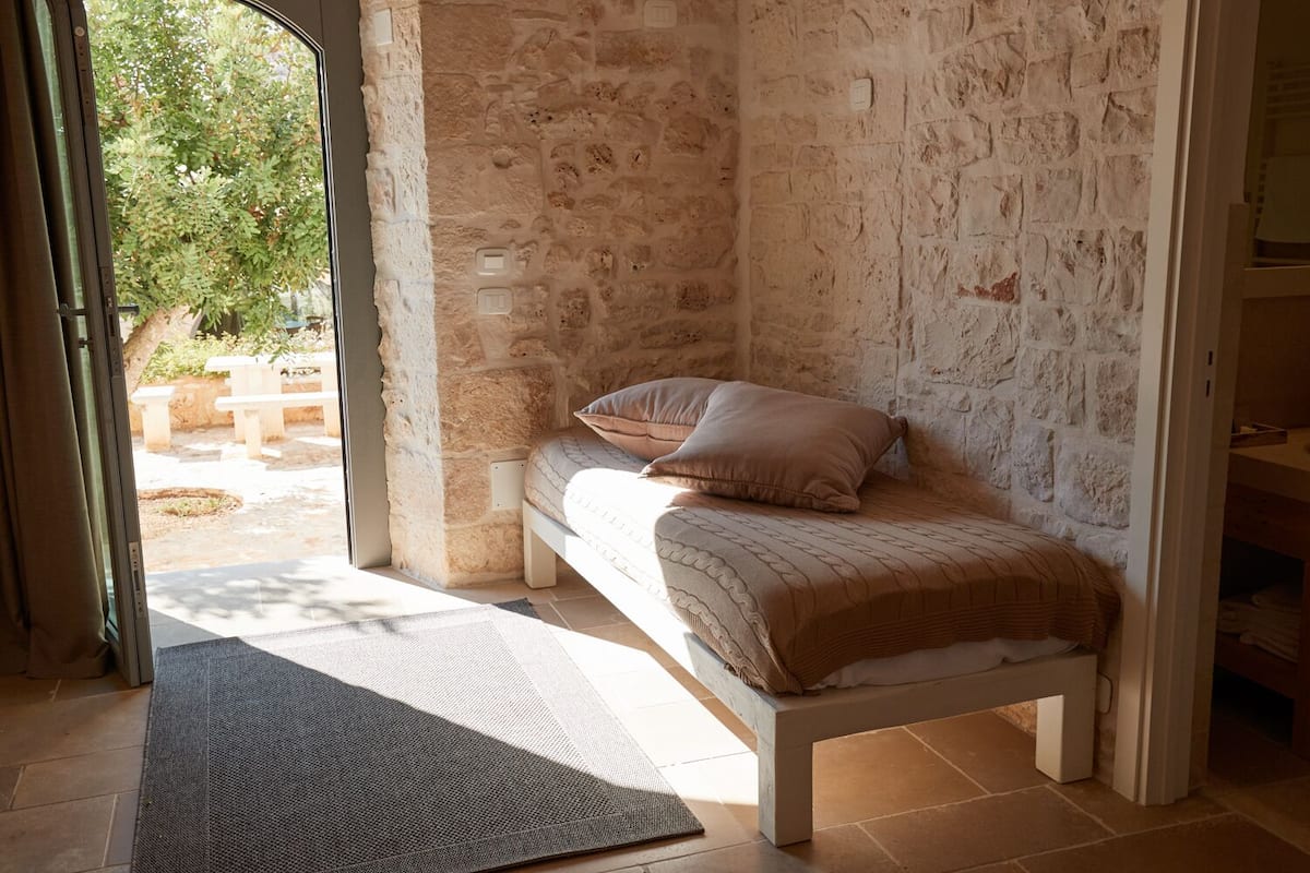 Une chambre avec un mur en pierre, un lit recouvert d’une couvre-lit à motifs et une vue sur l’extérieur.