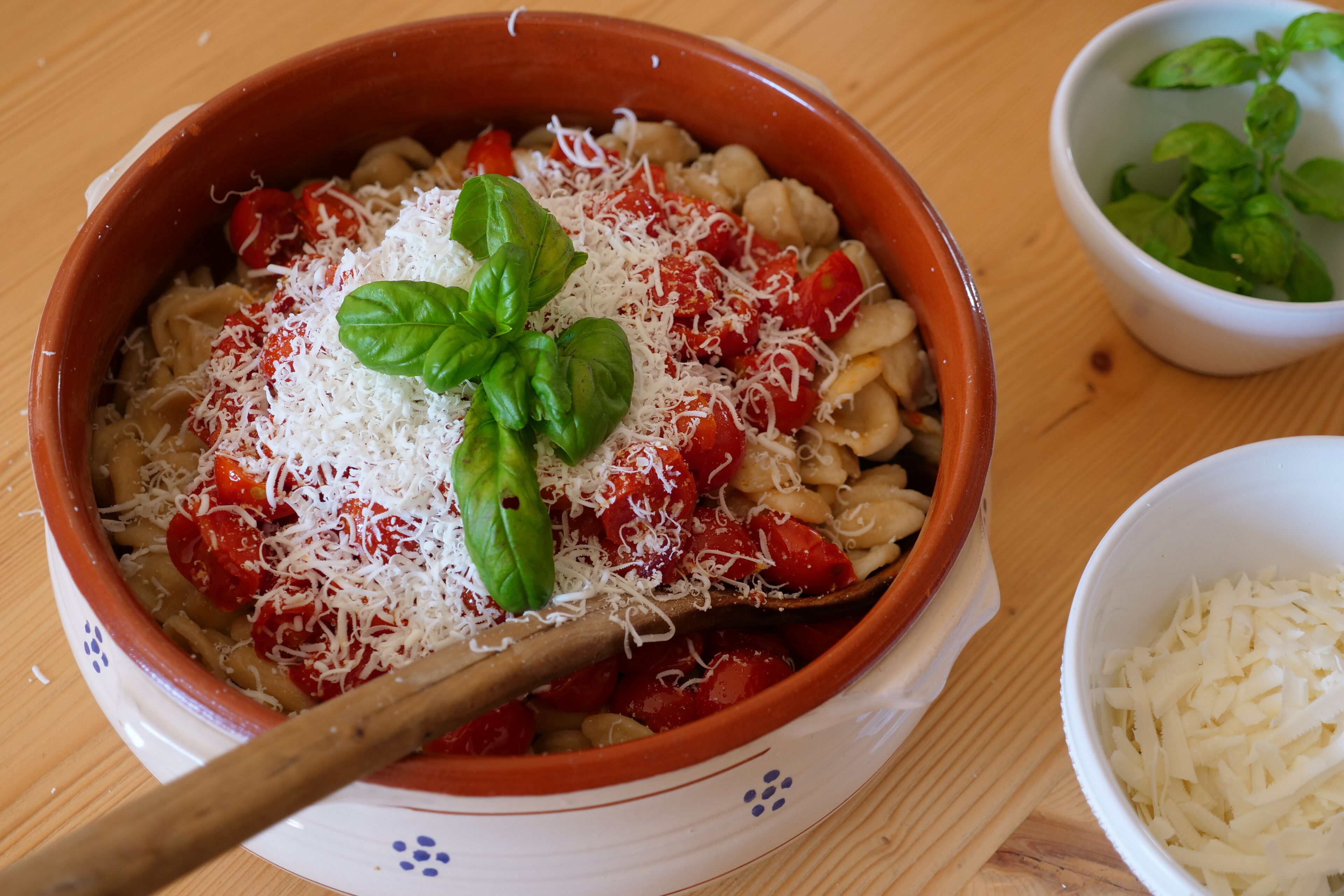 A bowl of pasta with tomato sauce, grated cheese, and basil on a wooden table.