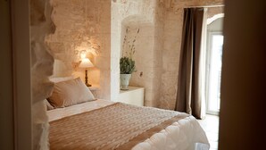 Een slaapkamer met een bakstenen muur, een bed met een beddengoed met een patroon, een bedlampje en een kamerplant.