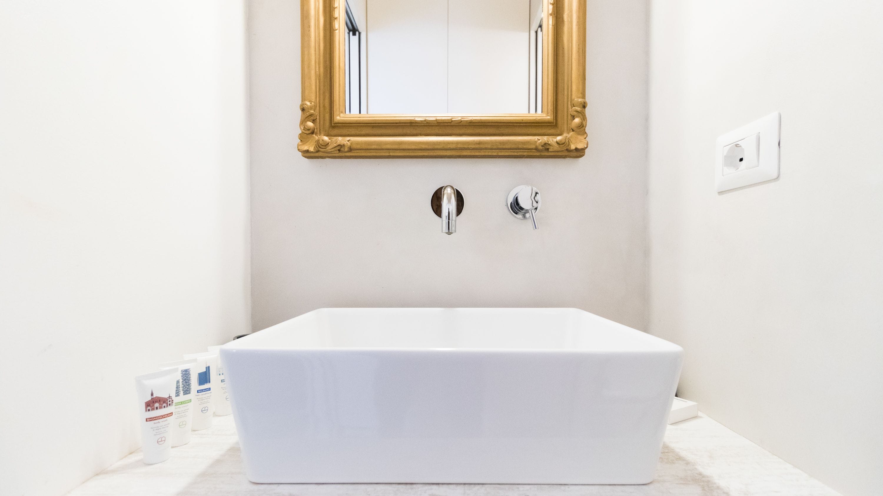 A bathroom with a white bathtub, a gold-framed mirror, and two faucets.