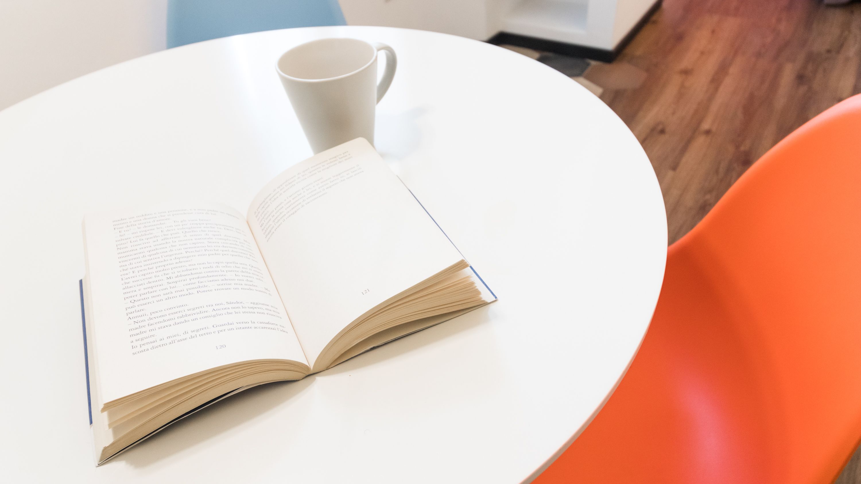 An open book on a white table with a white cup beside it.