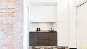 A compact kitchen with white cabinets, a dark countertop, and a brick wall. - Italianway   - Ciaia (Milan)