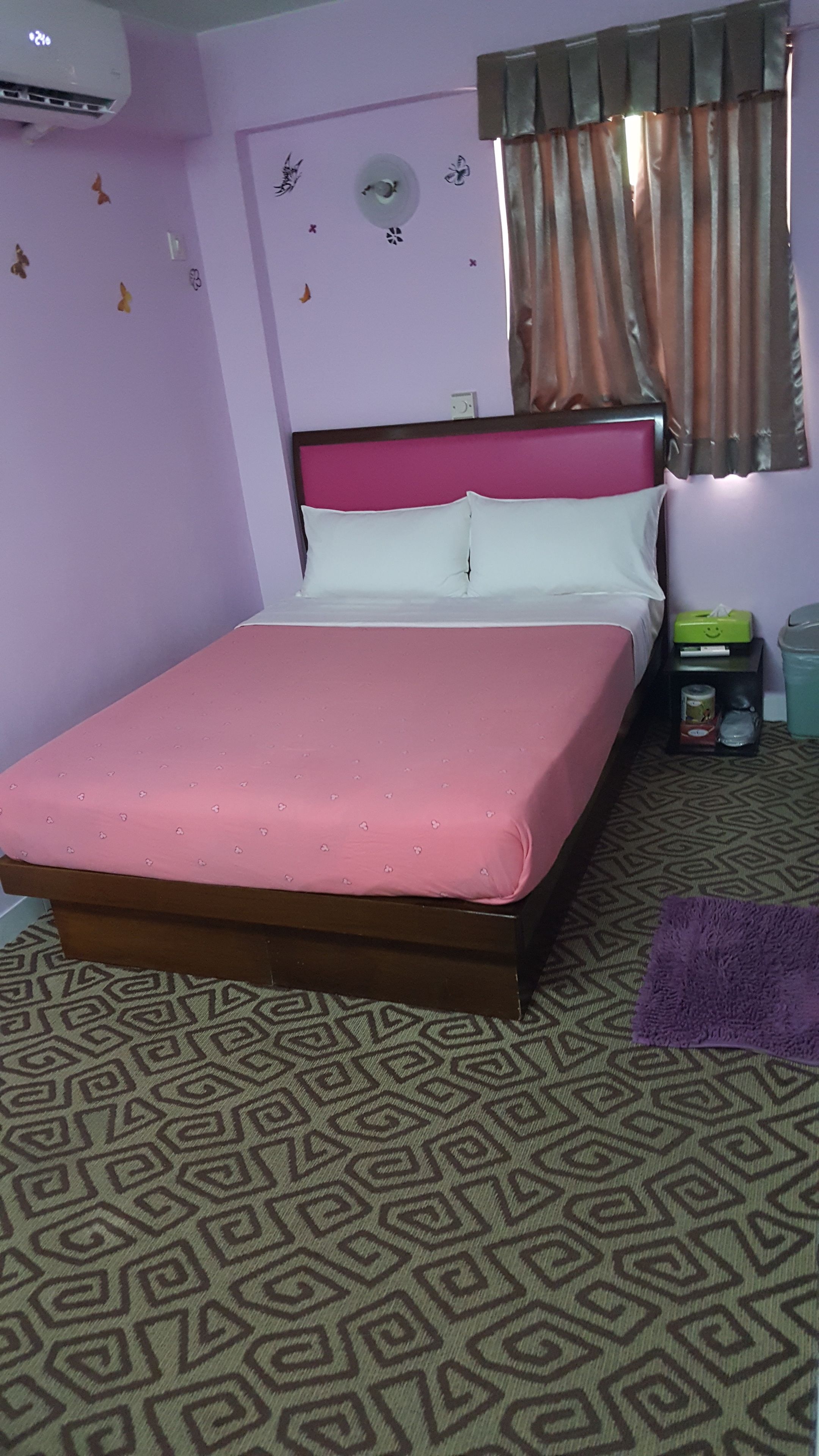 A bed with a pink bedspread, a headboard, and a wall-mounted air conditioner.
