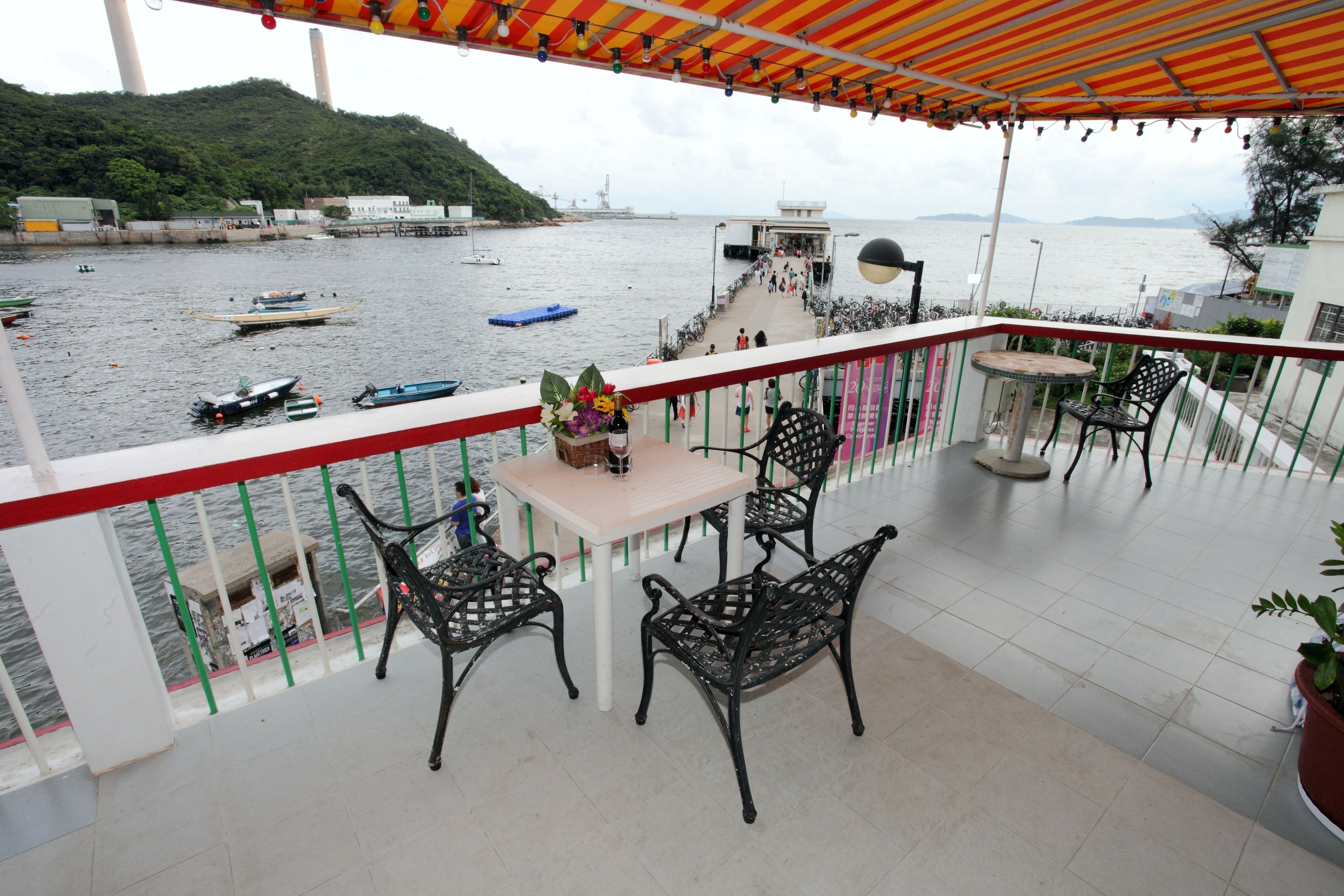 Ein Balkon mit Tisch und Stühlen, der auf ein Gewässer mit Booten und eine entfernte Hügelkulisse blickt.
