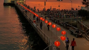 A pier with red lanterns, a boat docked on the left, and people walking along the pier. - Man Lai Wah Resort (Lamma Island)
