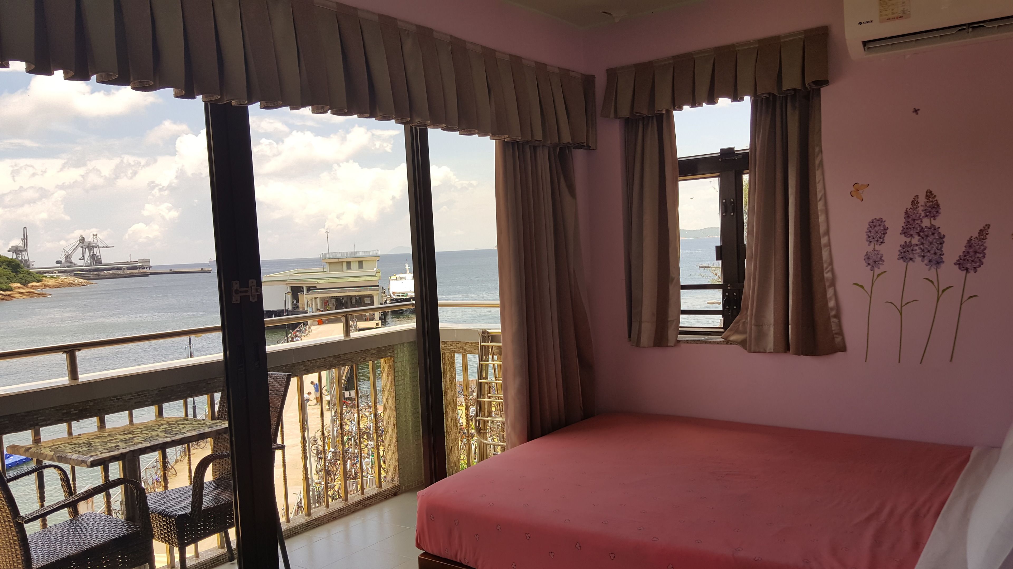 Una habitación con cama, balcón con barandilla y vistas al mar y al puerto.