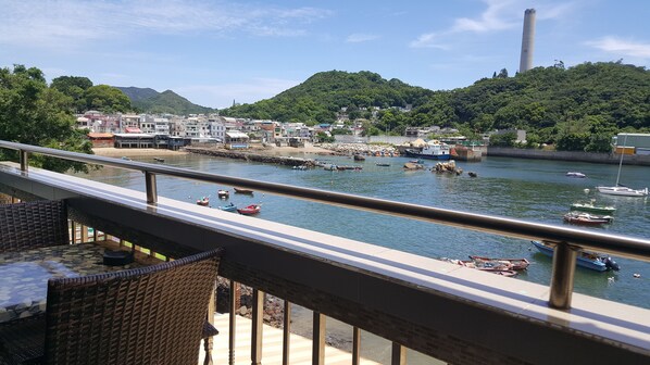 A balcony with wicker furniture overlooking a harbor with boats and a hillside town.