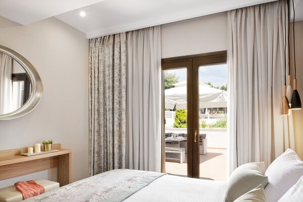 A modern hotel room with a bed, a wooden bedside table with decorative items, a large window with curtains, and a view of the outdoor area. - Hotel Simeon (Polygyros)
