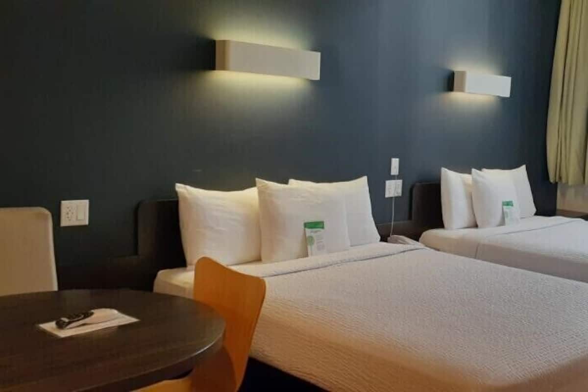 A hotel room with two beds, a small table, and a window with a view of buildings.