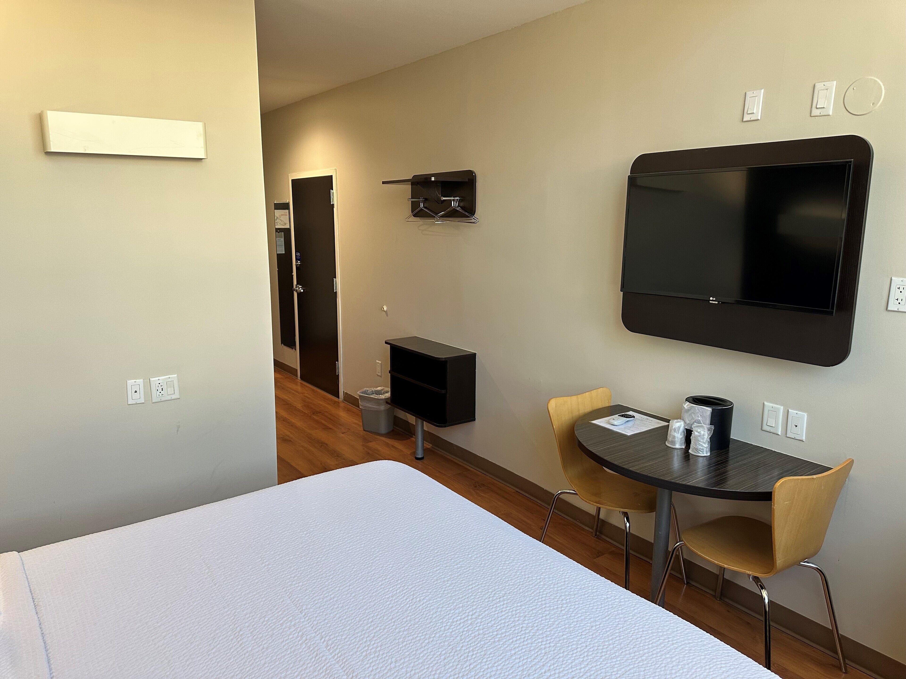 Una habitación de hotel con cama, escritorio con silla, televisor y un pequeño cubo de basura.