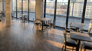 A modern restaurant with large windows, wooden flooring, and metal chairs.