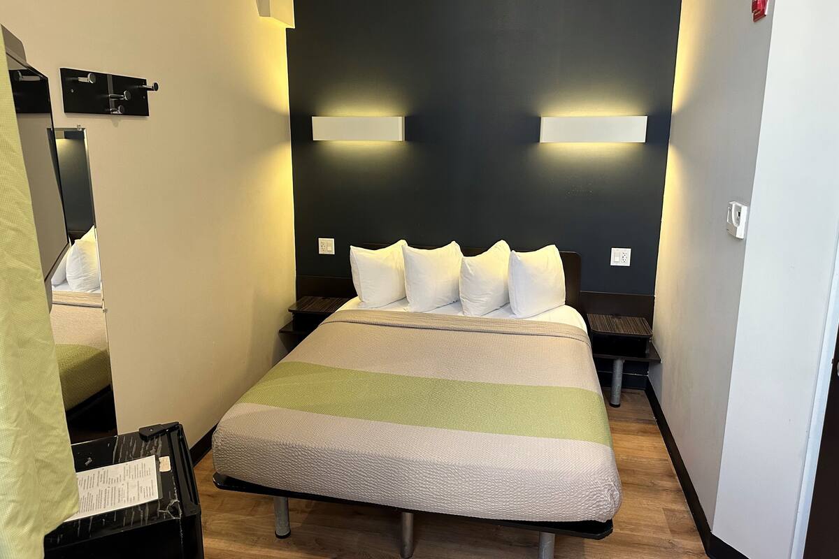 A hotel room with a bed, bedside tables, a mirror, and a wall-mounted light fixture.