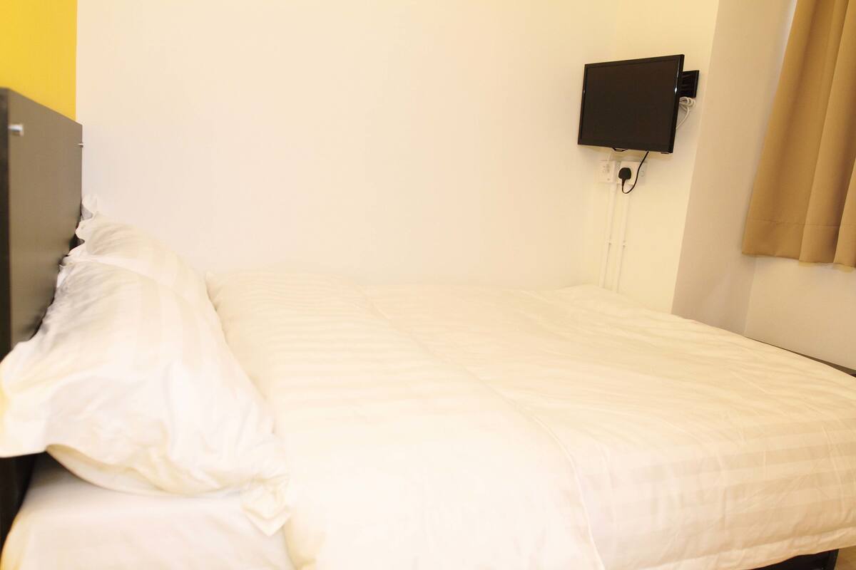 A single bed with white bedding in a room with a white wall and a black TV mounted on the wall.