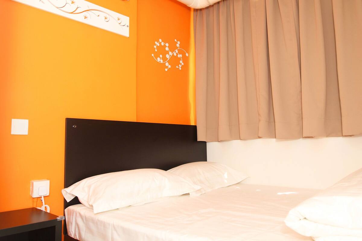 A hotel room with an orange wall, a black headboard, and a bed with white bedding.