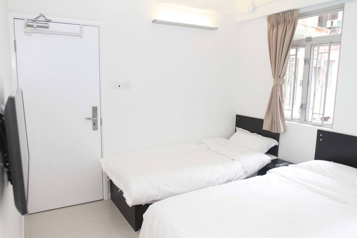 A hotel room with two single beds, a flat-screen TV, a door, and a window with curtains.