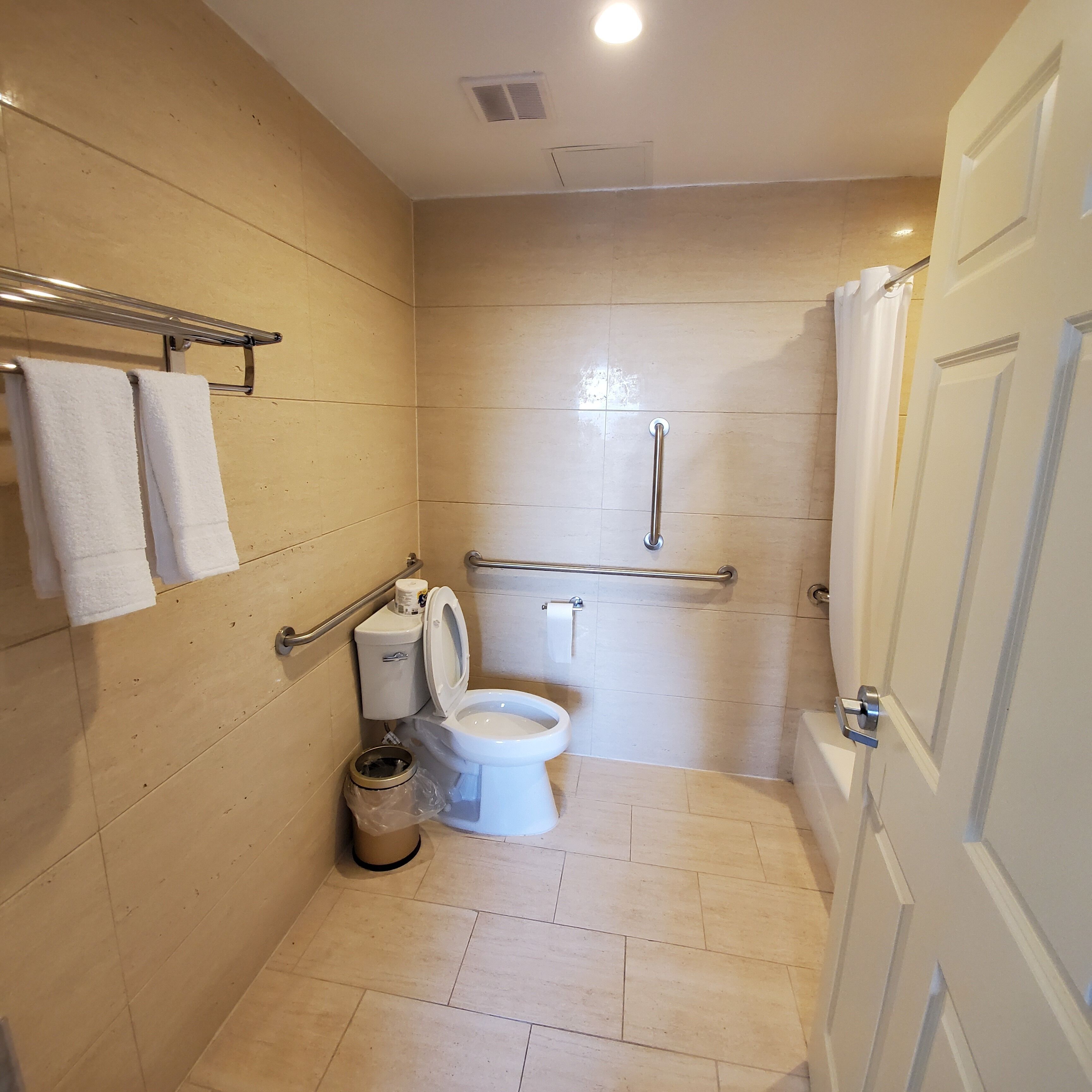 A small, modern bathroom with a toilet, handrail, and a trash can.
