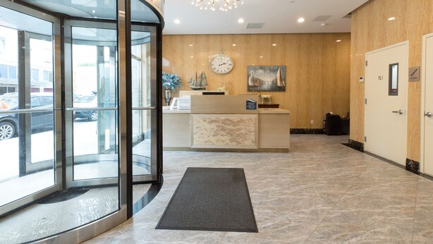 Eine Hotellobby mit einer Rezeption, einer Uhr, einer Kristallleuchtre und einem Glastür.