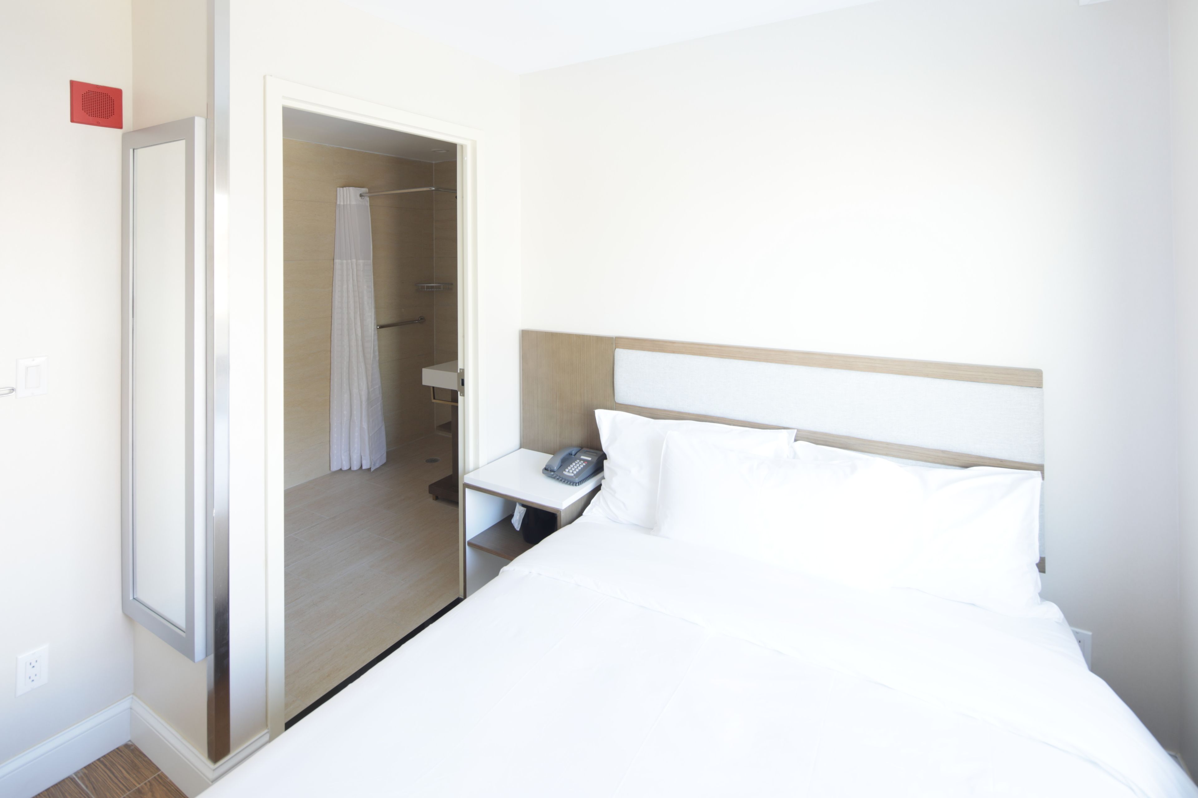 Habitació d'hotel amb un llit, un telèfon a la nit, una tauleta de nit i un bany amb cortina de dutxa.