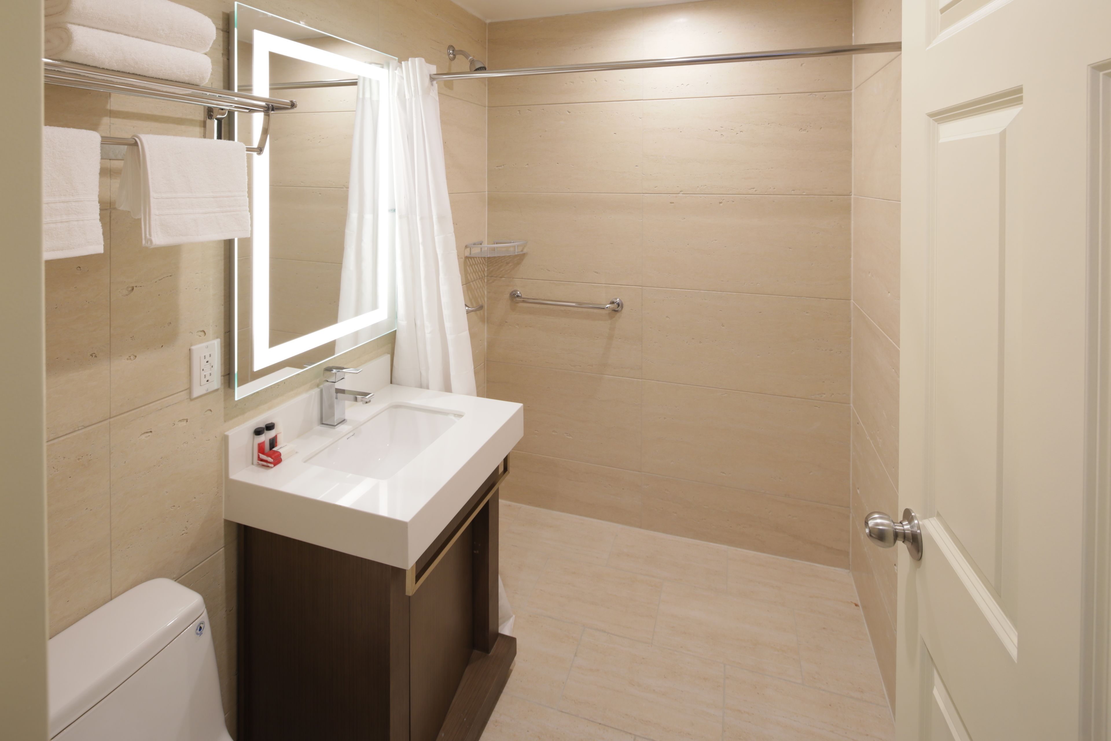 A modern bathroom with a white sink, a mirror, a shower with a glass door, and a towel rack with folded towels.