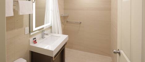 A modern bathroom with a white sink, a mirror, a shower with a glass door, and a towel rack with folded towels.