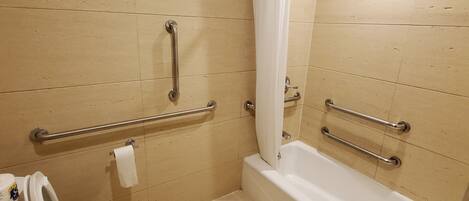 A bathroom with a toilet, a bathtub, and handrails.