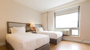 Ein Hotelzimmer mit zwei Betten, einem Nachttisch mit Lampe, einem großen Fenster mit Jalousien und einer Klimaanlage.