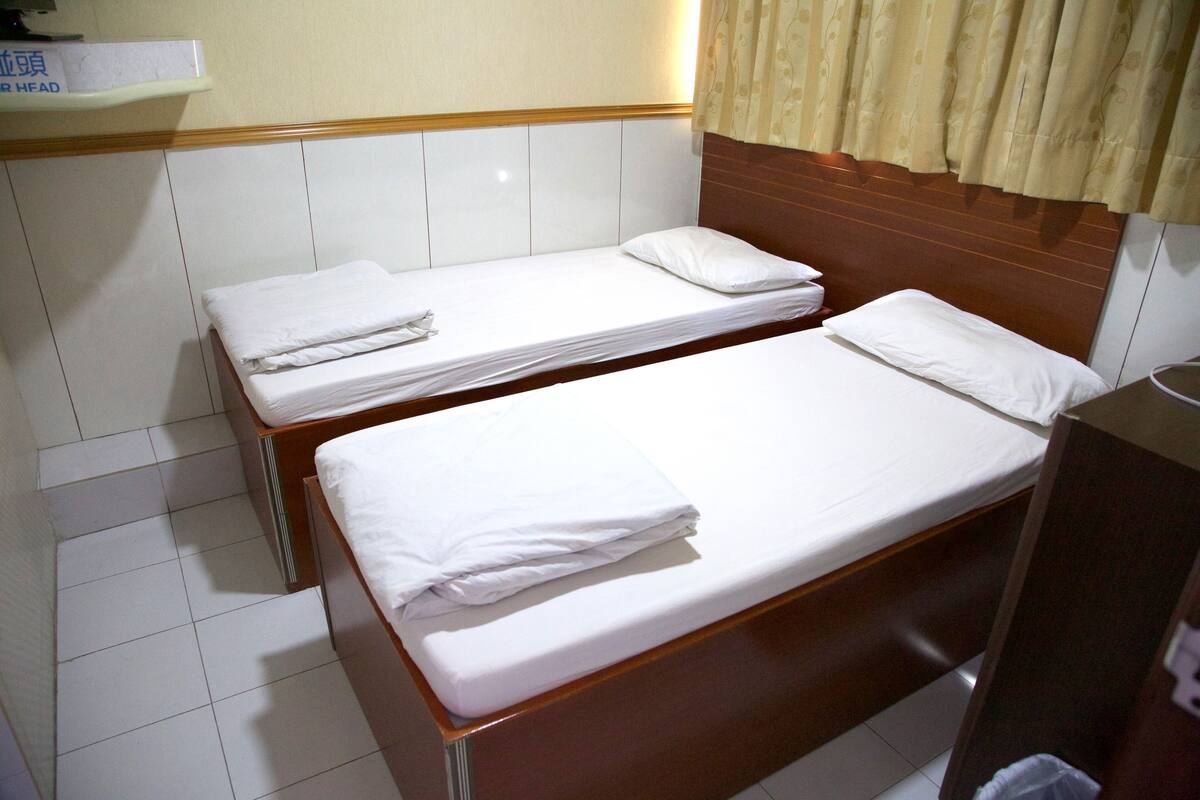 Two single beds with white linens in a room with a wooden headboard and a beige curtain.