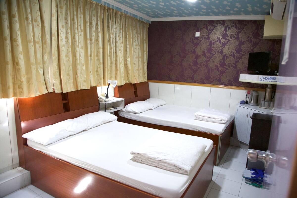 A hotel room with two beds, a small desk, a nightstand, a television, and a bathroom area.