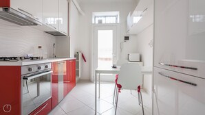 Een moderne keuken met witte kastjes, een rode kookeiland, roestvrijstalen apparatuur en een raam boven de spoelbak.