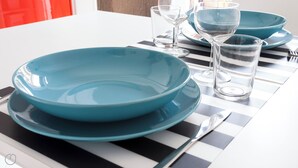 Een eettafel met blauwe borden, heldere glazen en een tafelkleed met strepen.